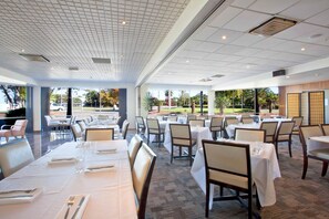 Un vaste espace dédié à la salle à manger, avec de nombreuses tables et chaises, de grandes fenêtres offrant une vue sur l’extérieur et un aménagement intérieur propre et moderne.