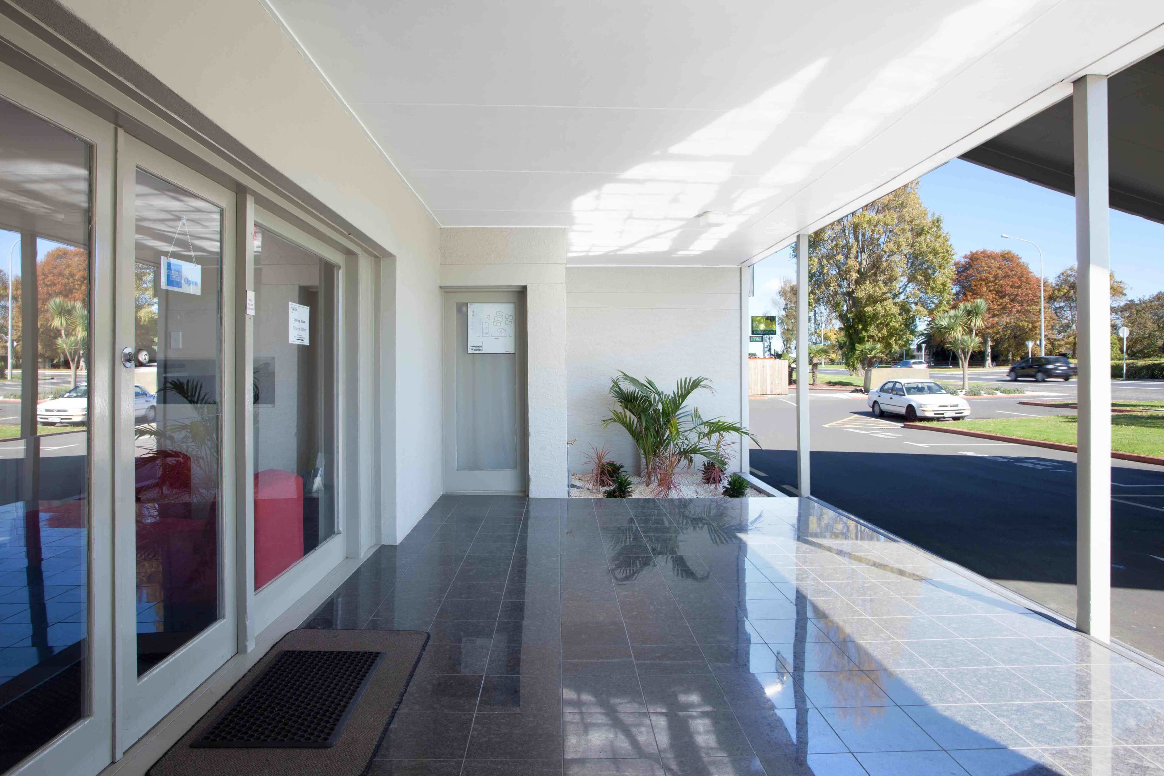A modern building entrance with a glass door, a small indoor plant area, and a view of the street outside.