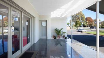 A modern building entrance with a glass door, a small indoor plant area, and a view of the street outside.