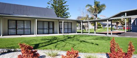 A modern building with a covered outdoor area, a well-maintained lawn, and decorative shrubs.