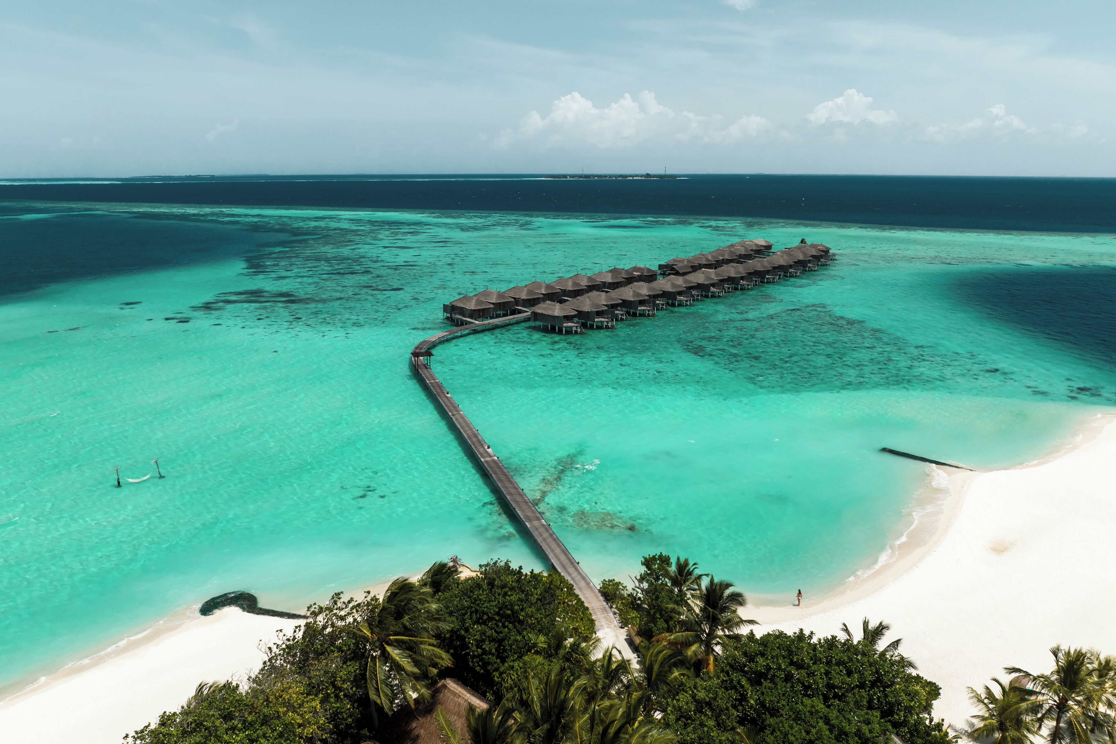 An overwater bungalows structure connected by a pier to a white sandy beach, surrounded by clear turquoise waters.