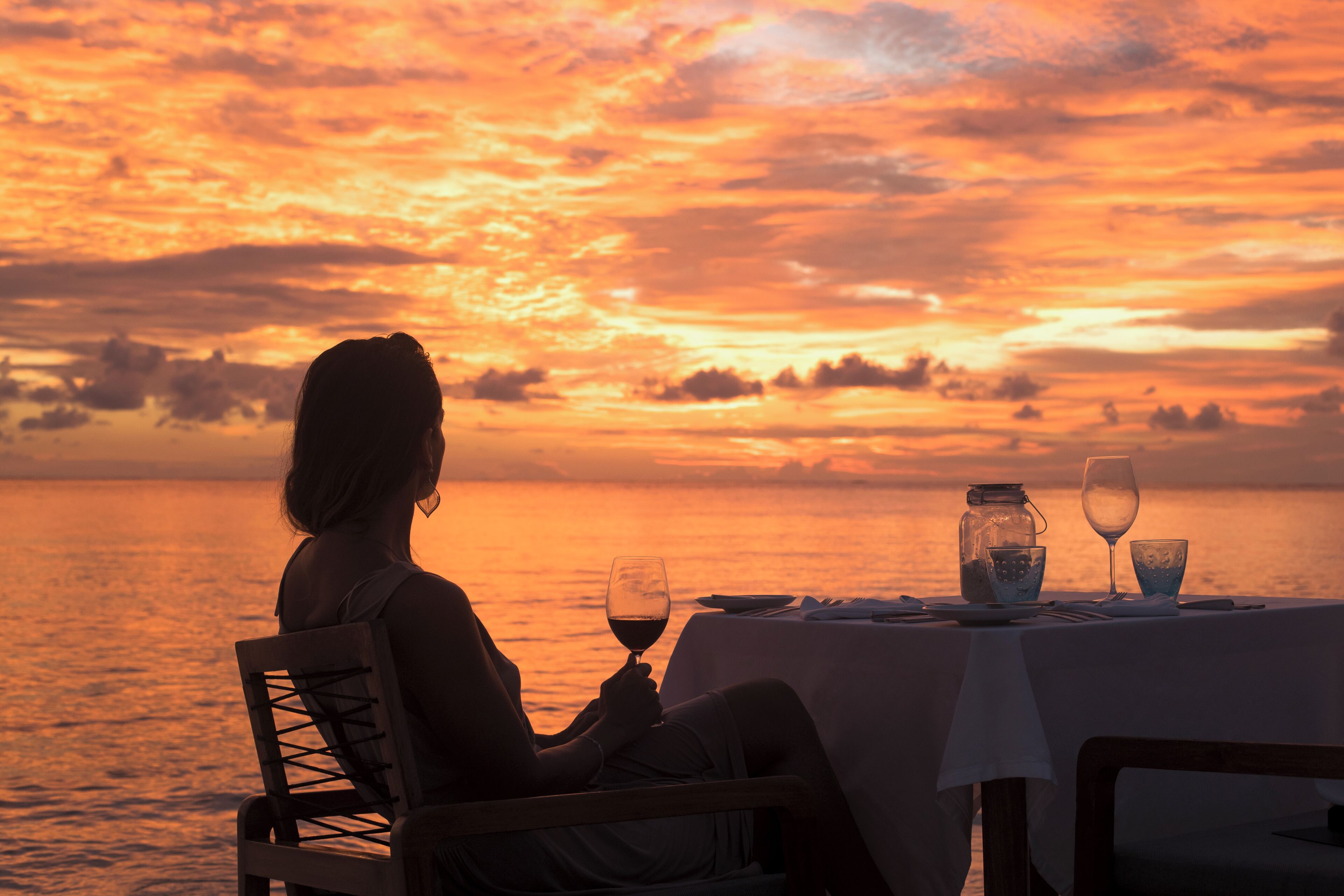 Una persona sentada a una mesa junto al agua al atardecer.