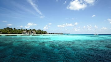 A clear view of a tropical beach resort with overwater bungalows and a boat in the distance.