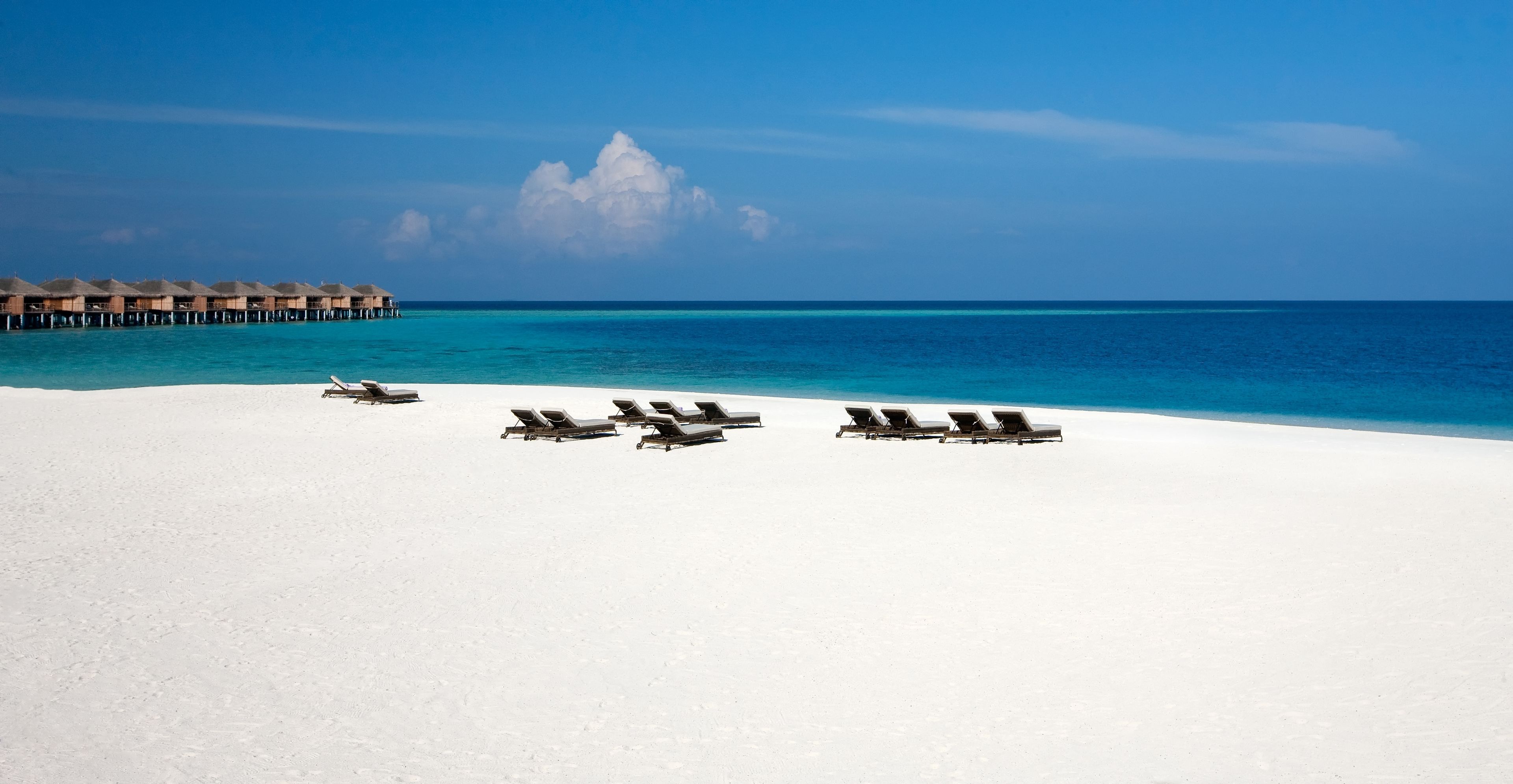 A beach with white sand and a row of sun loungers facing the ocean.