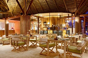 Un restaurante con mesas y sillas de madera, una zona de bar y un techo de paja.