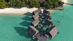 An overwater bungalow resort with multiple structures connected by a central walkway, surrounded by clear turquoise waters and a sandy beach. - Constance Moofushi All Inclusive (Moofushi Island)