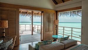 A room with a wooden floor, a bed, a table, and a view of the ocean. - Constance Moofushi All Inclusive (Moofushi Island)