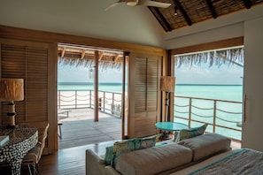 A room with a wooden floor, a bed, a table, and a view of the ocean. - Constance Moofushi All Inclusive (Moofushi Island)