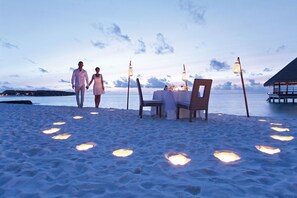 Un paisaje de playa con una mesa para dos, rodeada de arena y piedras luminosas.