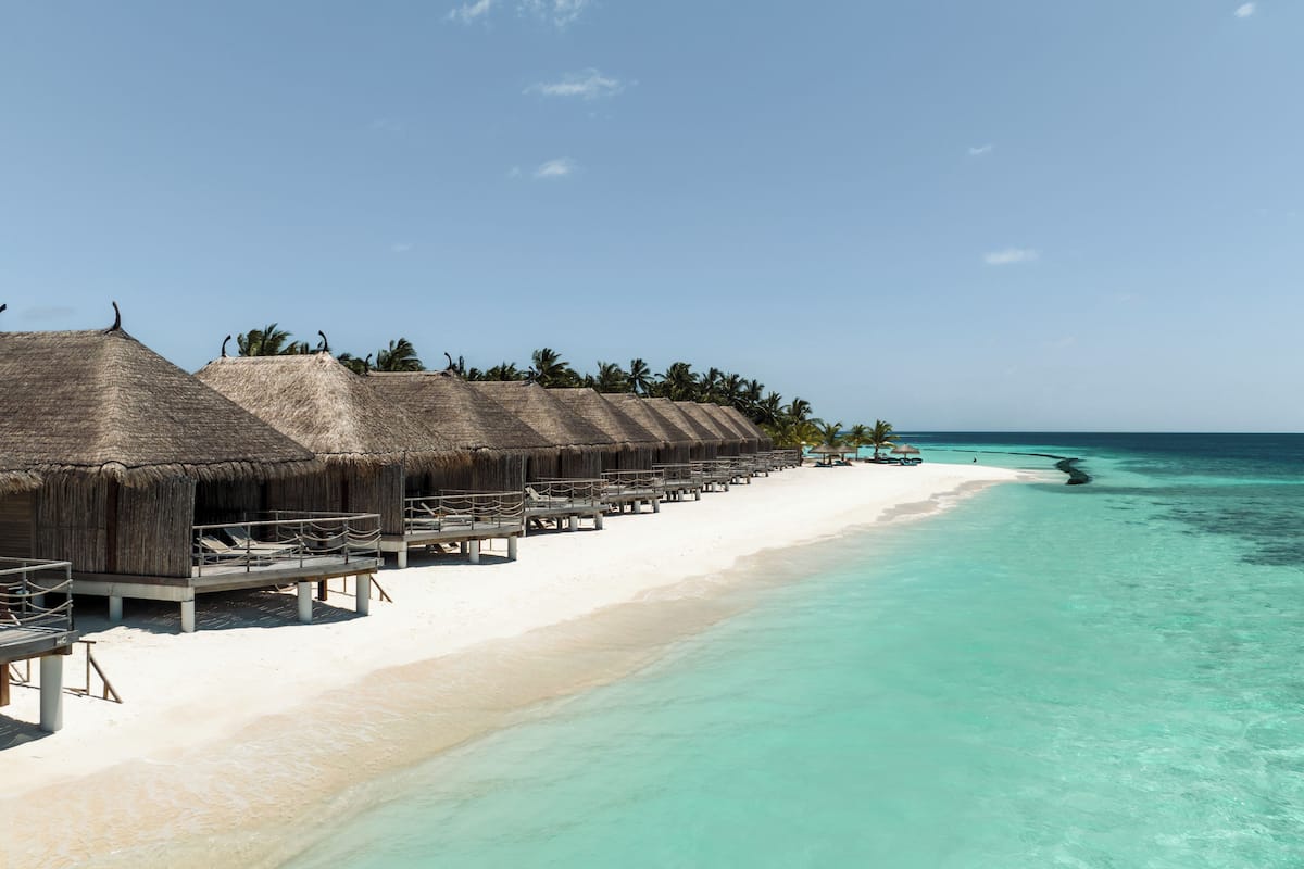 Cabañas sobre el agua con techos de paja, una playa de arena blanca y aguas turquesas.