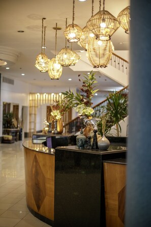 A reception area with a curved wooden reception desk, multiple hanging wicker chandeliers, and several potted plants. - The Bellavista Hotel (Lapu-Lapu)