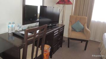 Una habitación de hotel con televisión, escritorio, silla, lámpara y cama.