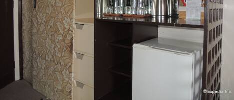 Habitación de hotel con minibar, refrigerador y un espejo que refleja el interior de la habitación.