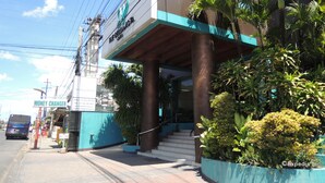 Un hotel con fachada moderna, entrada visible y zona de estacionamiento.