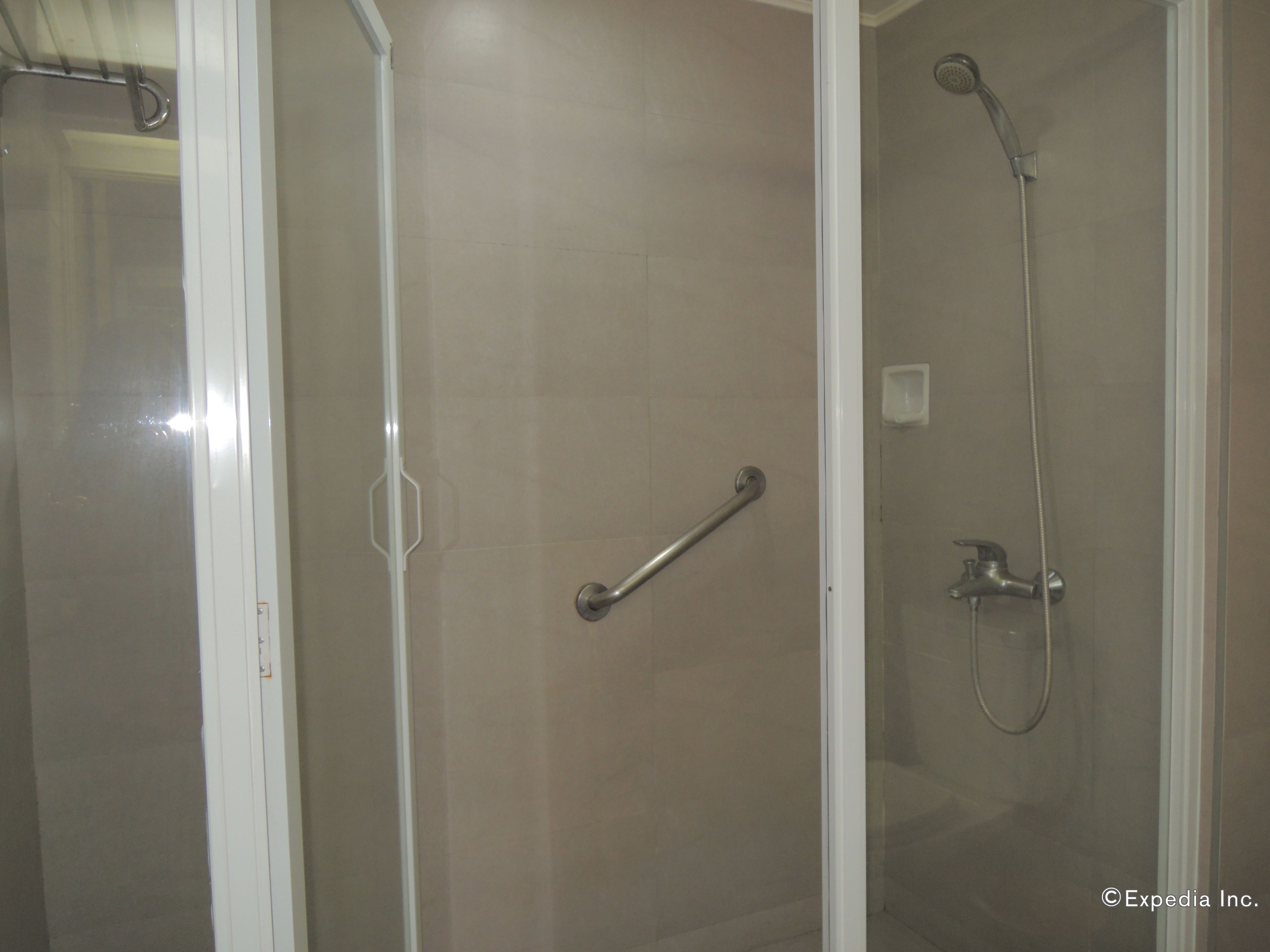 A shower area with a glass door, a handheld showerhead, and a wall-mounted faucet.