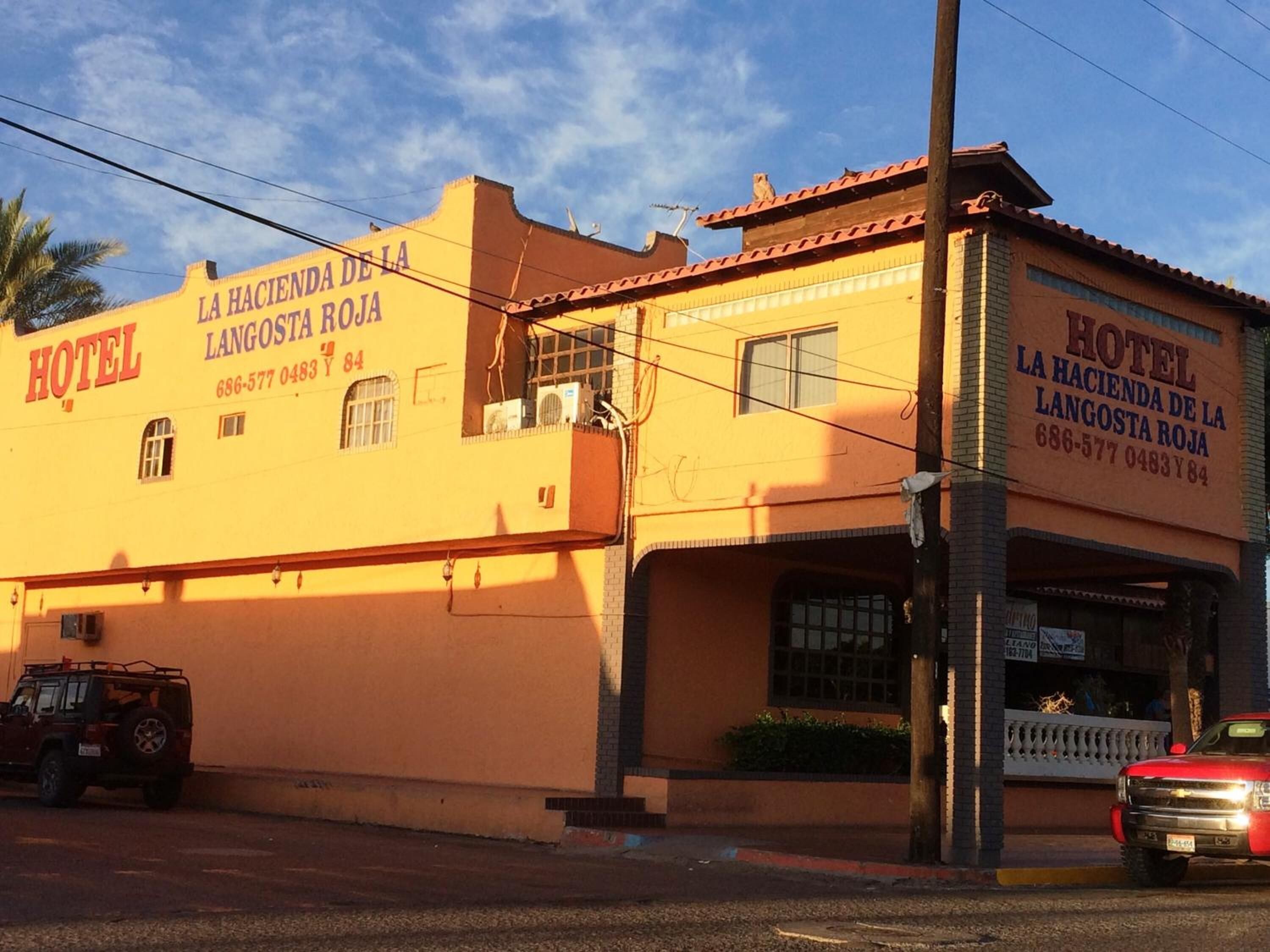 Un bâtiment à deux étages avec une enseigne indiquant « HÔTEL LA HACIENDA DE LA LANGOSTA ROJA » et un numéro de téléphone.