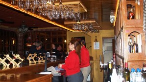 Zona de bar con estantes de madera, botellas de vino y copas colgantes.