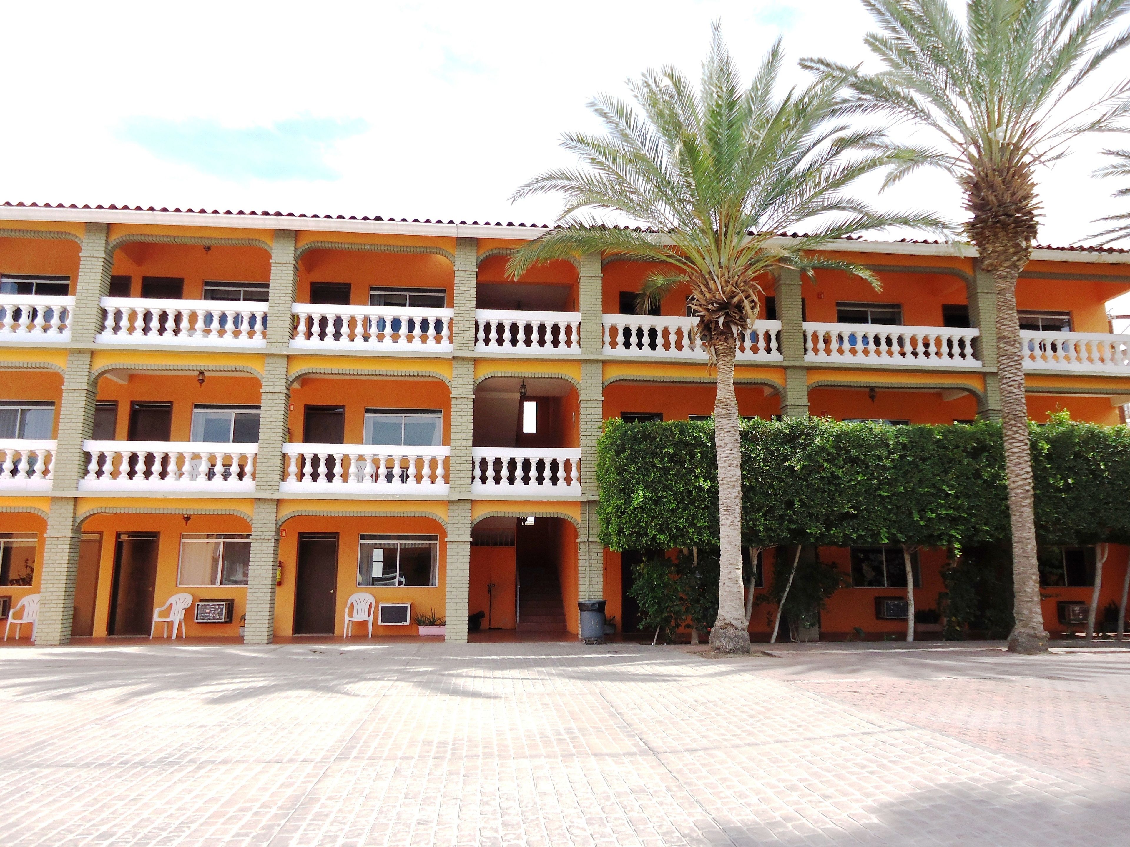Un edificio de varios pisos con balcones, un patio empedrado y palmeras.