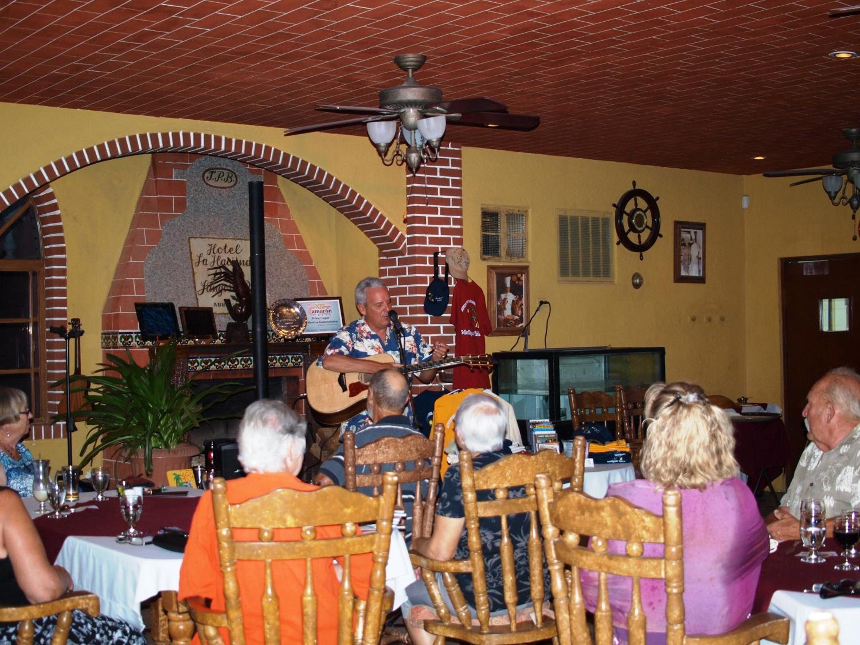 A restaurant interior with a brick wall, a stage for live music, and patrons seated at tables.