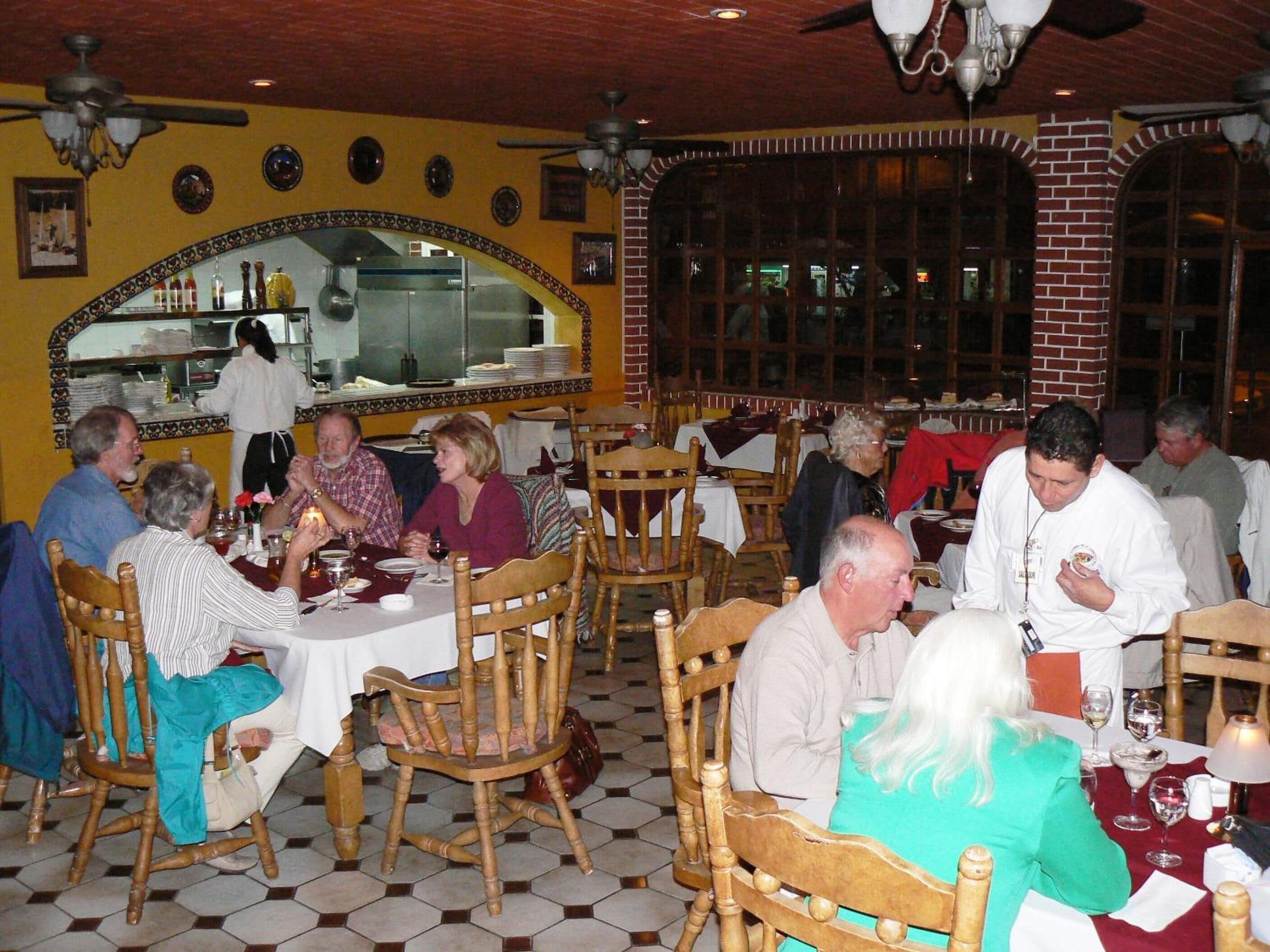 A restaurant with wooden chairs and tables, a tiled floor, and a brick wall.