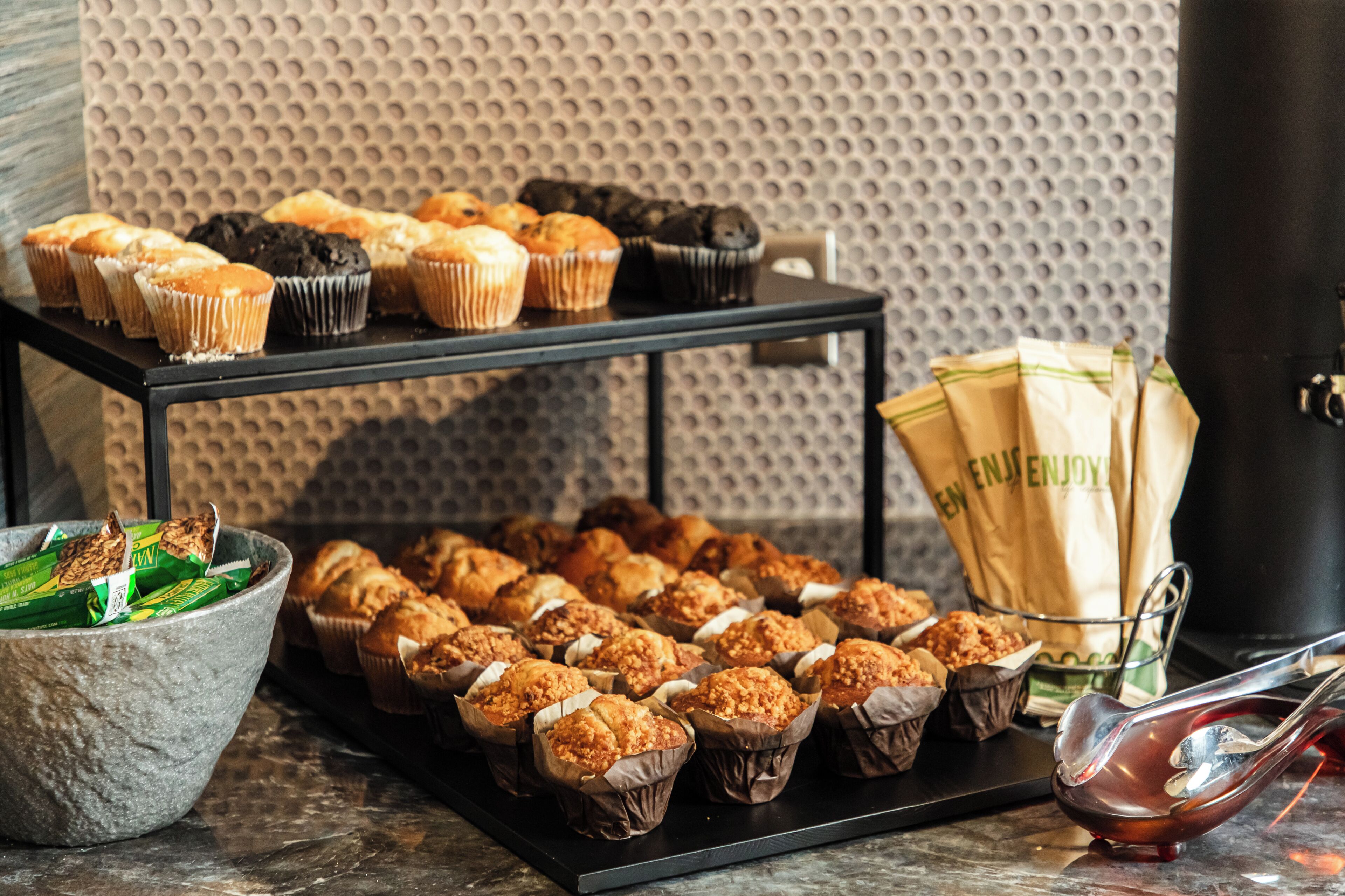A display of muffins and pastries on a table with a textured wall in the background.