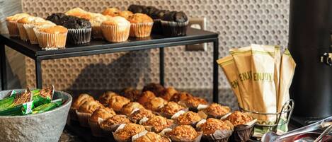 A display of muffins and pastries on a table with a textured wall in the background.