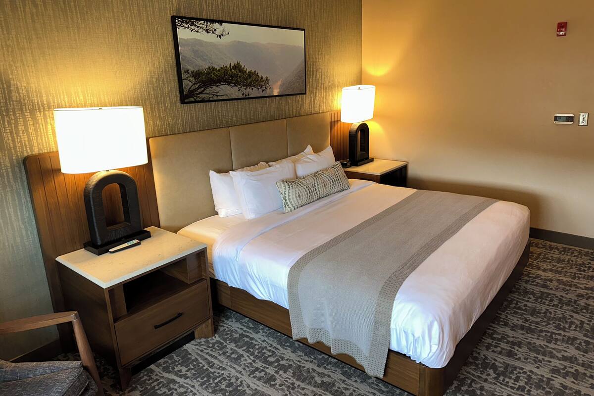 Ein Hotelzimmer mit einem großen Bett, zwei Nachttischen, einer Lampe, einem Gemälde und einem Rauchmelder.
