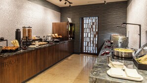 Een moderne keuken met een marmeren aanrechtblad, houten keukenkastjes en een buffet met diverse soorten eten.