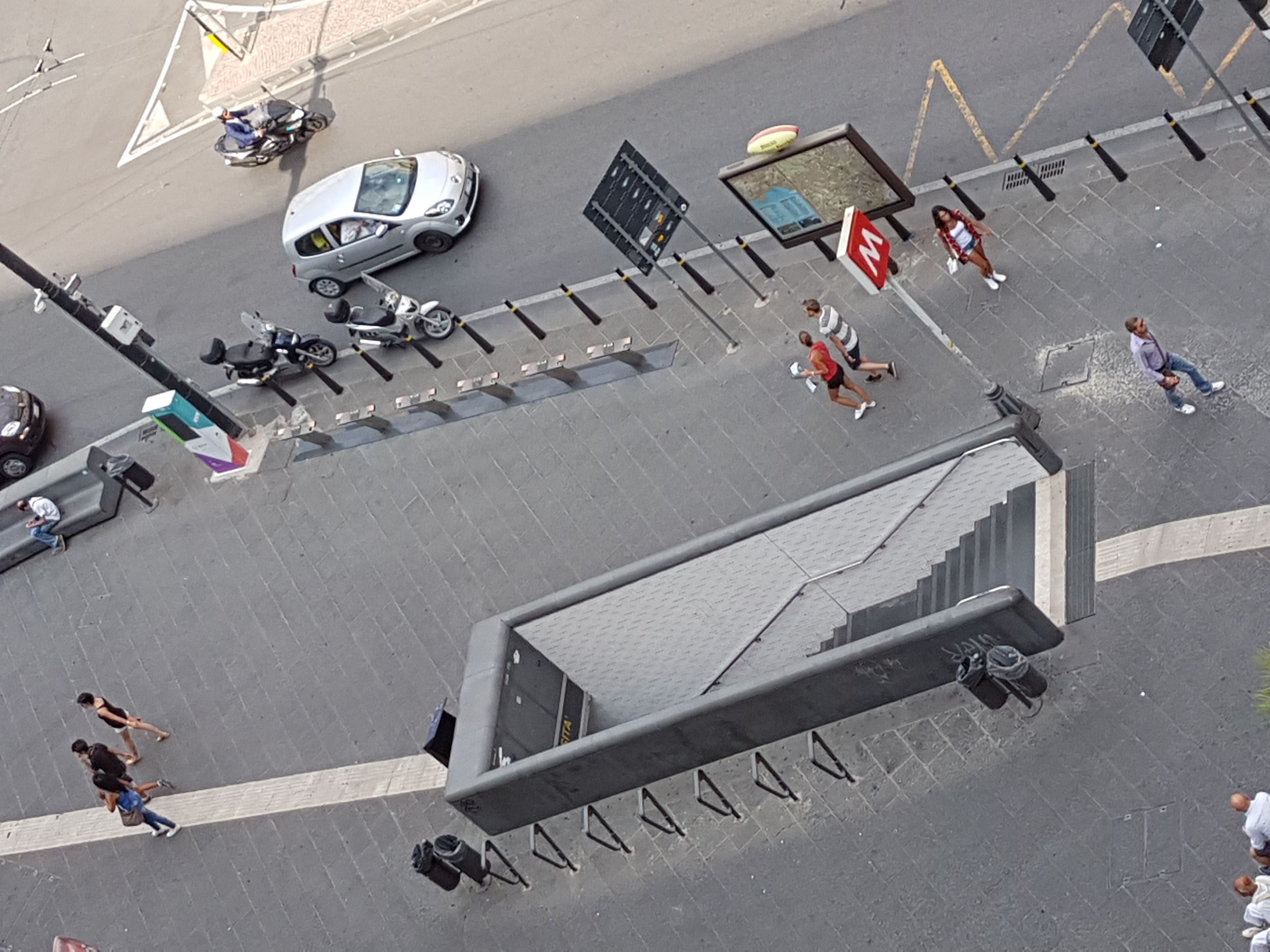 Vista aérea de una calle urbana con un paso de peatones, un coche y una parada de autobús.