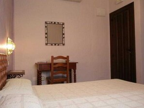 A bedroom with a bed, a wooden desk, a chair, a mirror, and a door. - El Soto de Roma (Fuente Vaqueros)