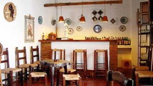 A rustic dining area with wooden chairs and a table, a brick fireplace, and various decorative plates on the wall. - El Soto de Roma (Fuente Vaqueros)