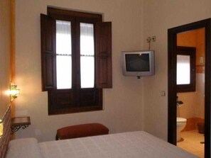 A bedroom with a bed, a television mounted on the wall, a window with wooden shutters, and a door leading to a bathroom. - El Soto de Roma (Fuente Vaqueros)