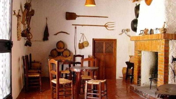 A rustic room with wooden furniture, a fireplace, and various wall decorations including a mounted animal head and tools. - El Soto de Roma (Fuente Vaqueros)