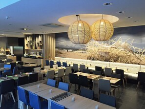 A modern restaurant with a beach mural, blue chairs, and hanging light fixtures. - Ostend Hotel (Ostend)