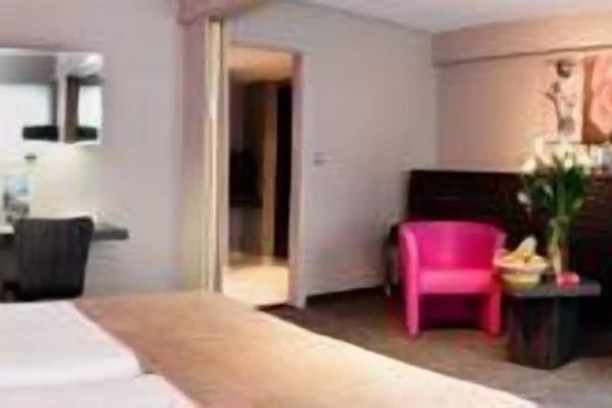 A hotel room with a bed, a desk, a chair, and a small table with a vase of flowers.