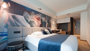 A hotel room with a large bed, a desk, and a chair. There is a painting on the wall and a sign with the word "EUWPO". - Ostend Hotel (Ostend)