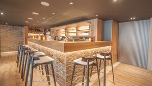 A modern bar area with a stone accent wall, wooden counter, and bar stools. - Ostend Hotel (Ostend)