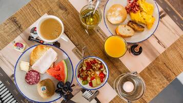 A breakfast table with plates of toast, eggs, bacon, and fruit. There is a cup of coffee and a glass of orange juice.