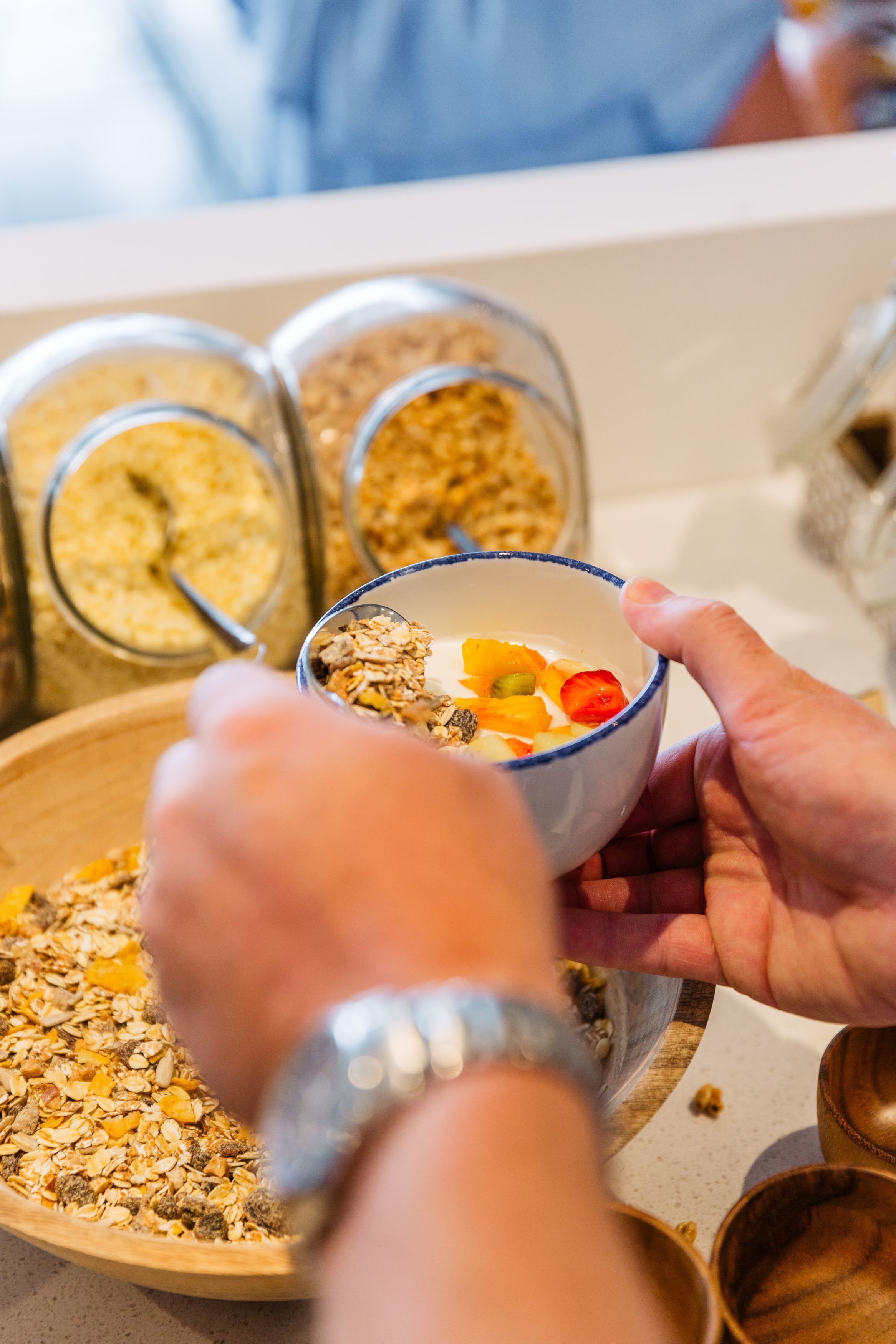 Eine Person hält eine Schüssel mit Granola und Früchten, im Hintergrund stehen Gläser mit Granola.