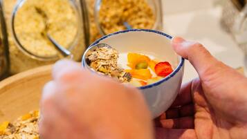 A person holding a bowl with granola and fruits, with jars of granola in the background.