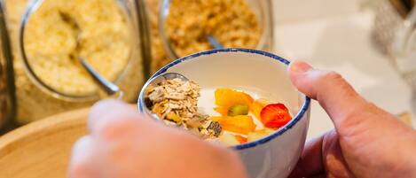 A person holding a bowl with granola and fruits, with jars of granola in the background.