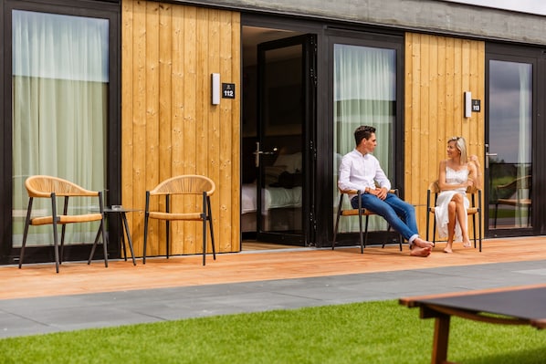 A modern hotel with wooden paneling and glass doors, numbered rooms 112 and 113, and outdoor seating with wicker chairs. - C-Hotels Zeegalm (Middelkerke)