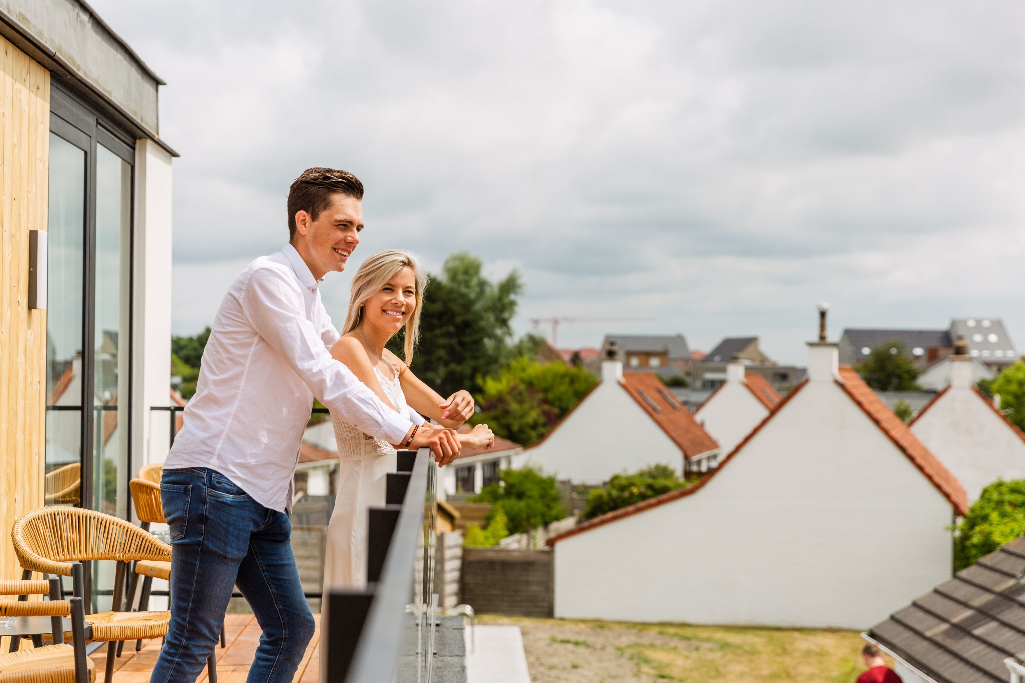 Una pareja parada en un balcón con vistas a edificios residenciales y un cielo nublado.