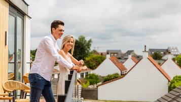 Una pareja parada en un balcón con vistas a edificios residenciales y un cielo nublado.
