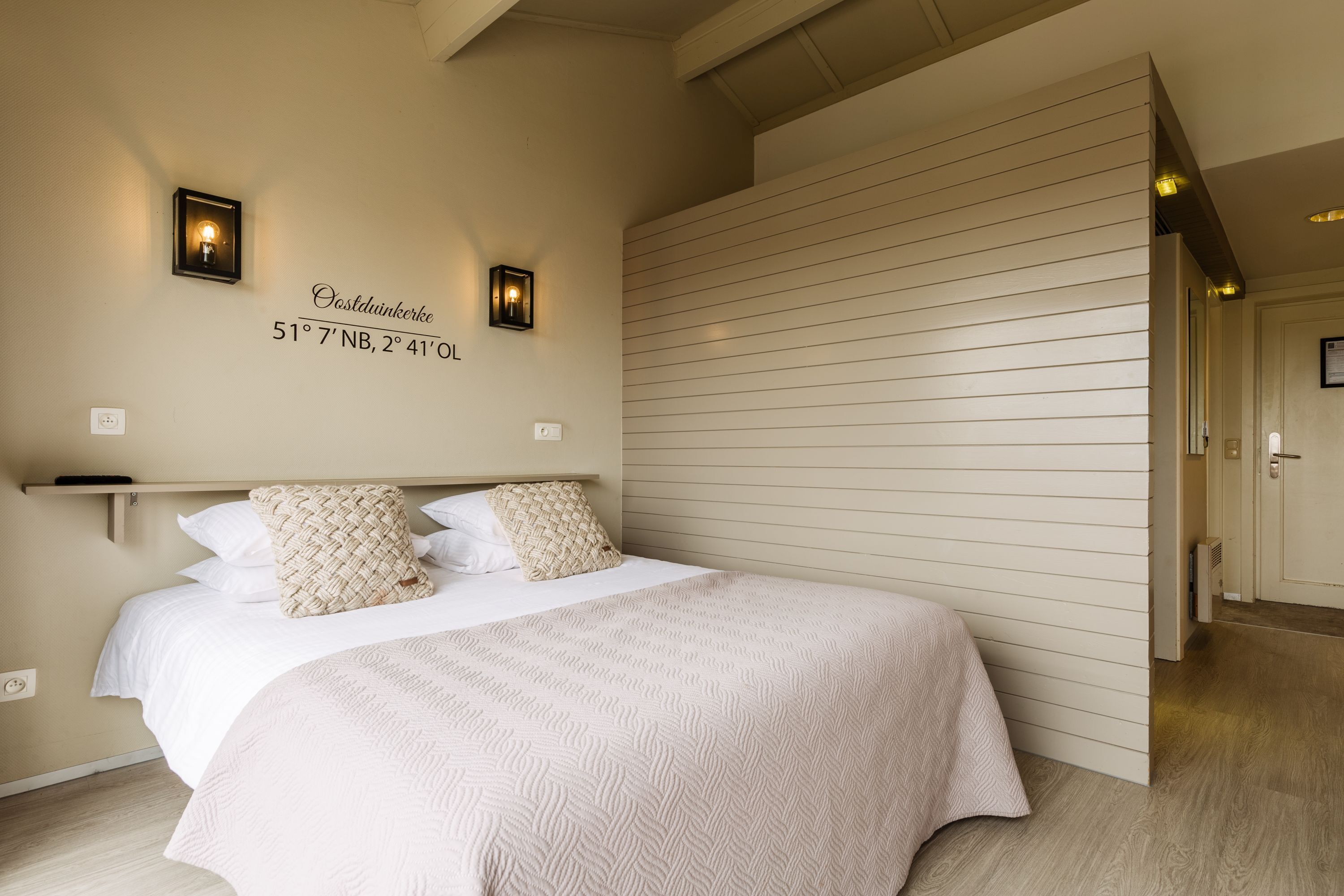 A bedroom with a bed, two wall-mounted lights, and a wall-mounted sign with coordinates.