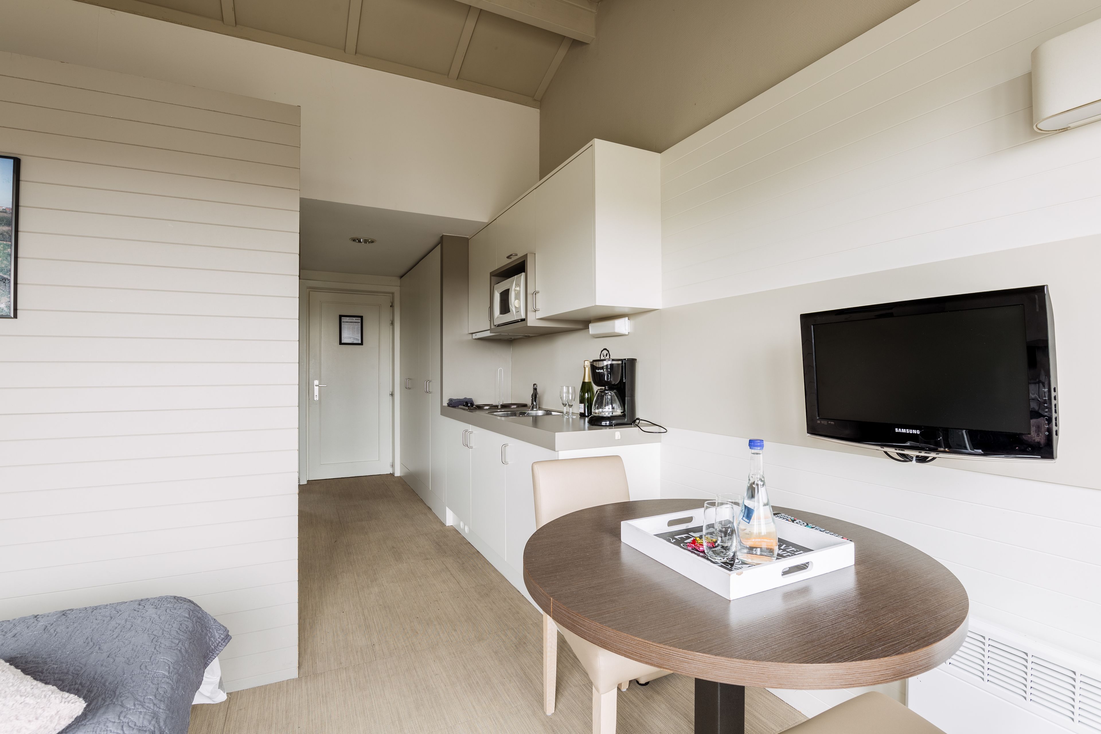 A modern hotel room with a dining area, kitchenette, and a flat-screen TV.
