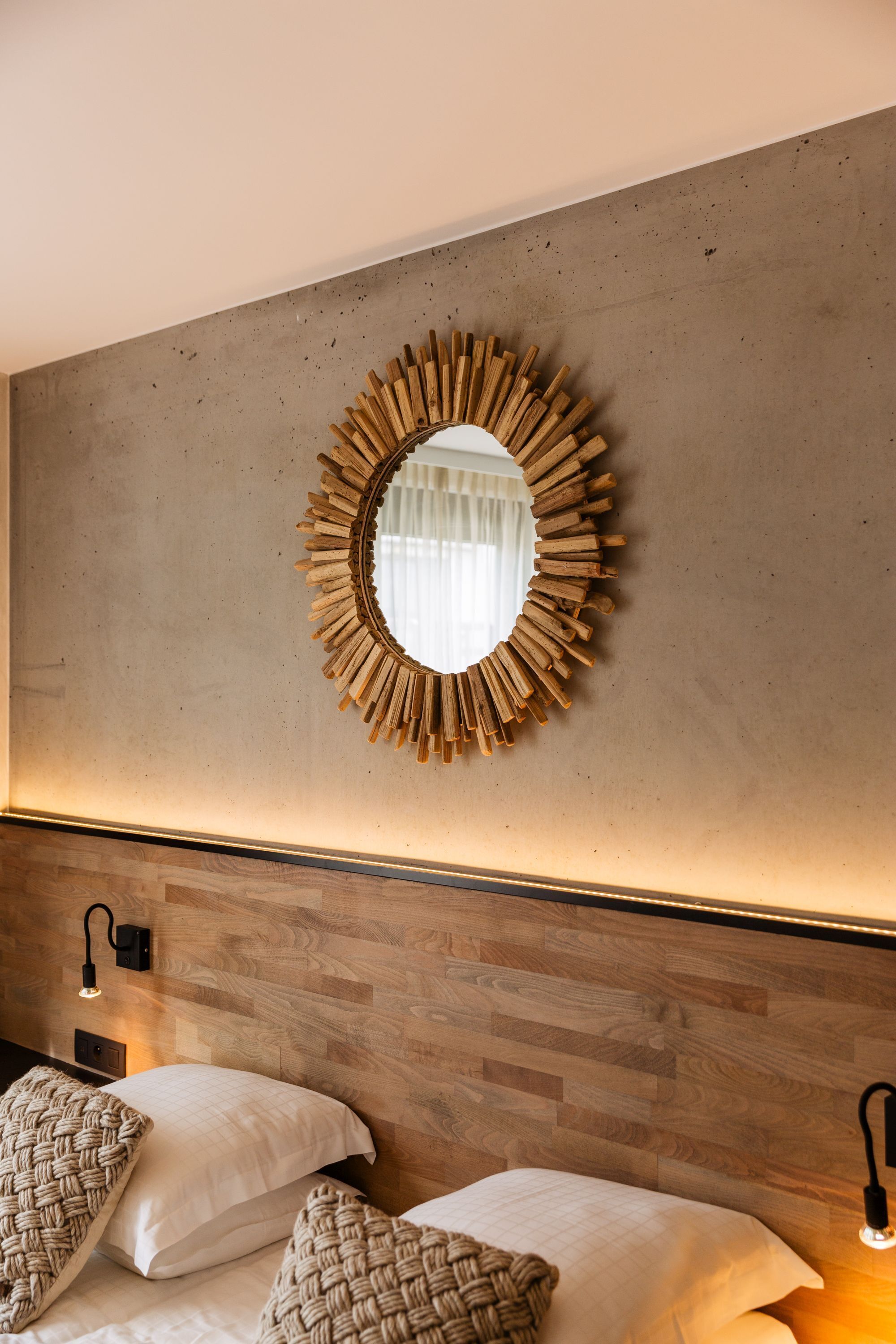 Un dormitorio con cabecera de madera, un espejo redondo con marco de madera y dos lámparas de noche.