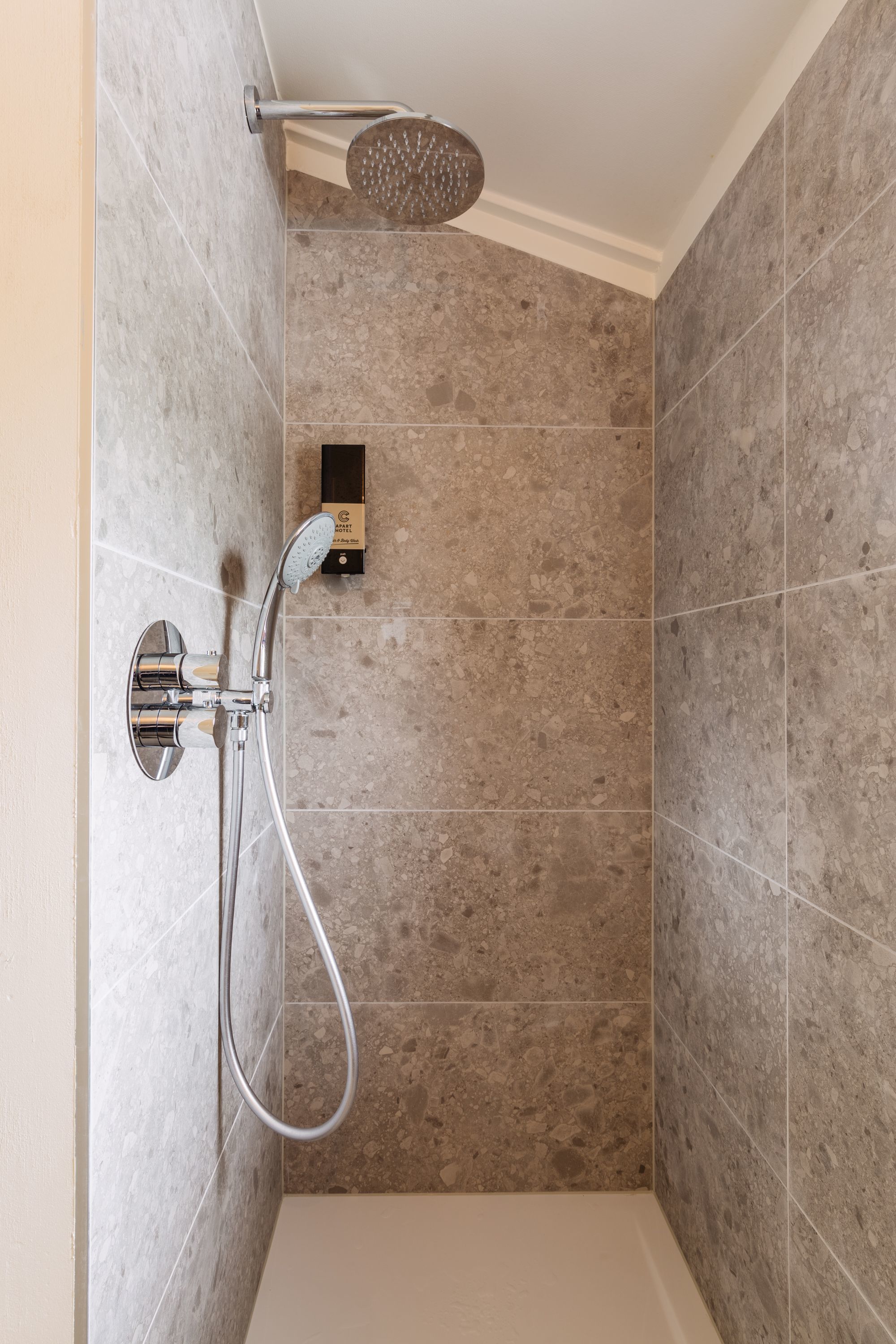A shower area with a handheld showerhead and a wall-mounted control panel.