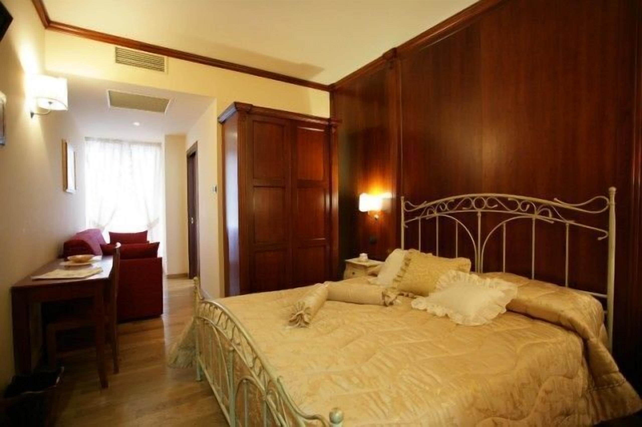 Habitación de hotel con una cama grande, cabecera de madera, un escritorio con una silla y un ventanal con cortinas.