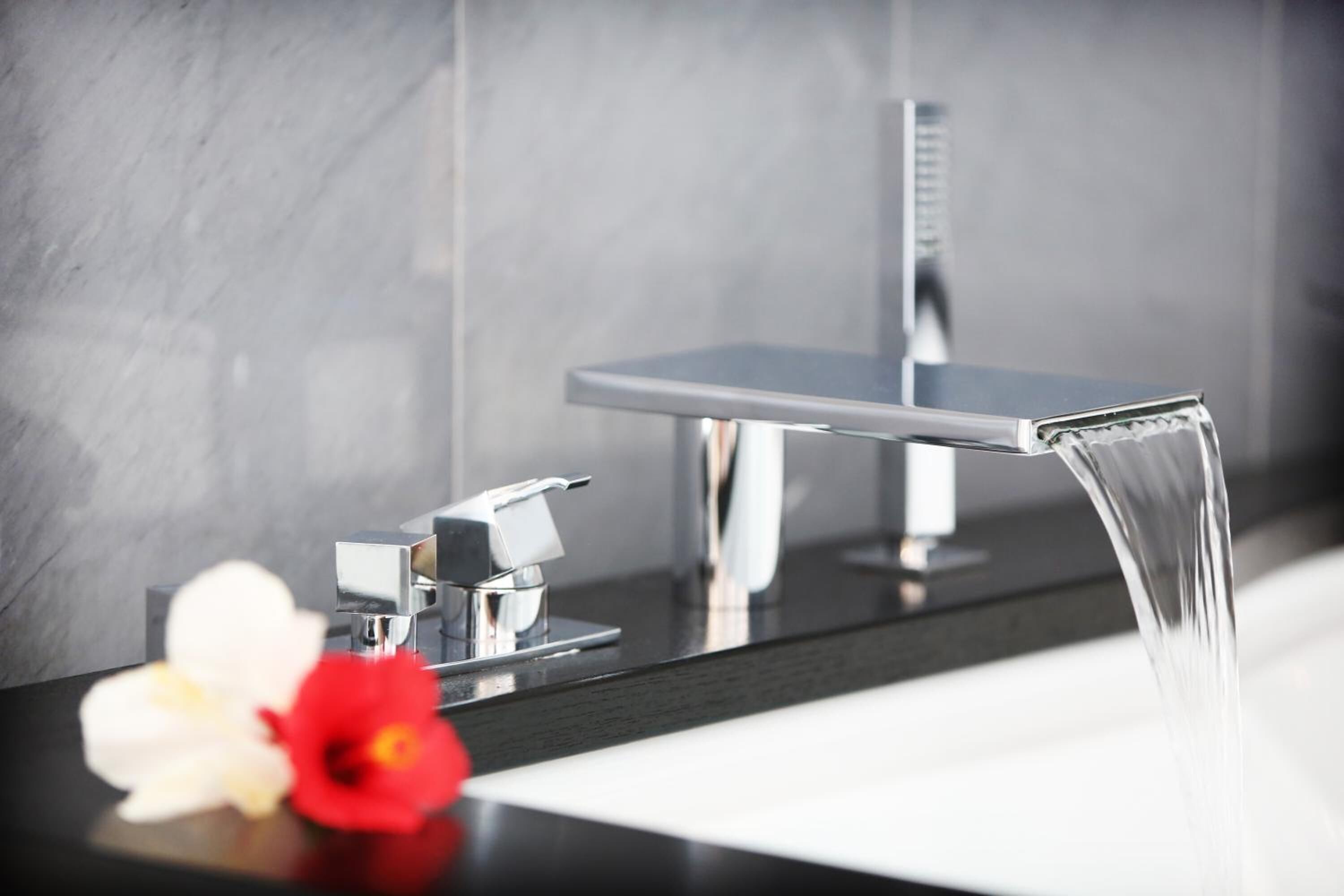 Une salle de bain moderne avec un robinet élégant, un miroir et une fleur posée sur le comptoir.